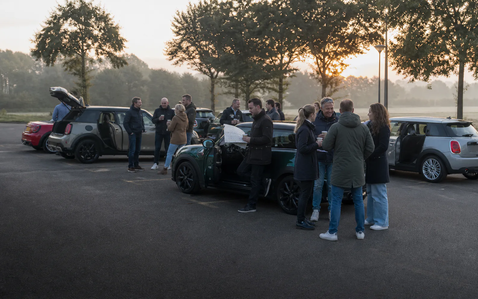 Deelnemers drinken koffie en begroeten elkaar bij geparkeerde MINI's voor vertrek